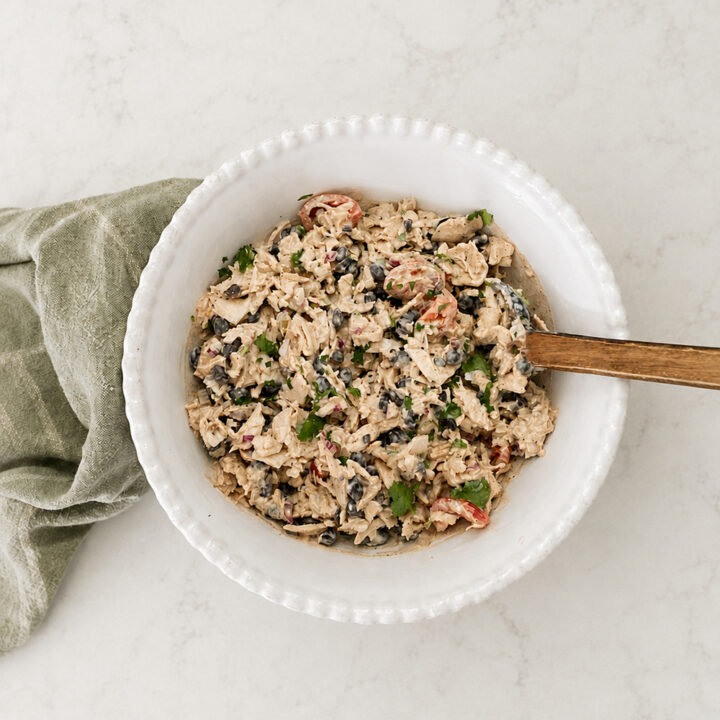 Homemade Southwest chicken salad with black beans, cherry tomatoes, cilantro, and shredded chicken served in a white ceramic bowl.