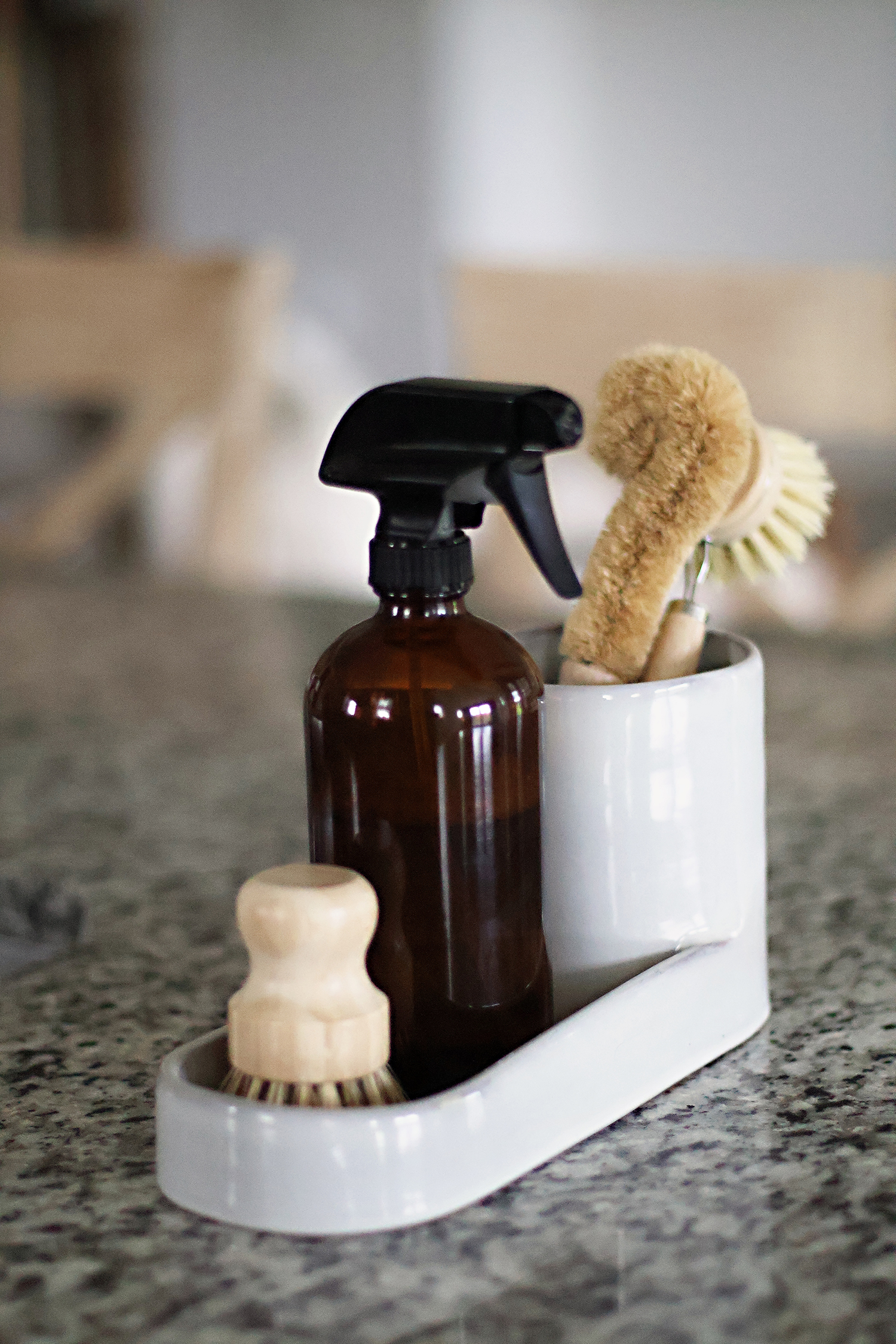 Minimal kitchen sink accessories including an amber glass spray bottle and natural cleaning brushes.